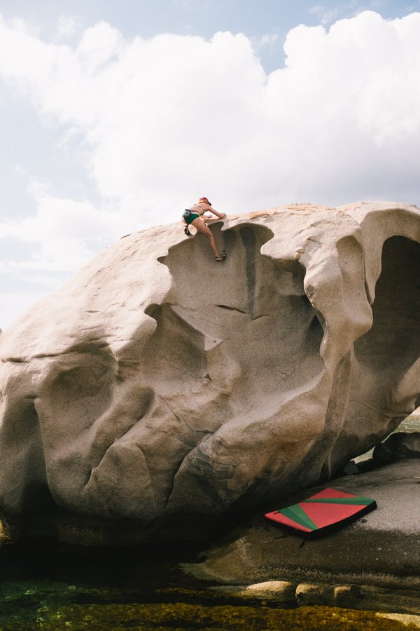 Woman climbing a big granite boulder by the sea
